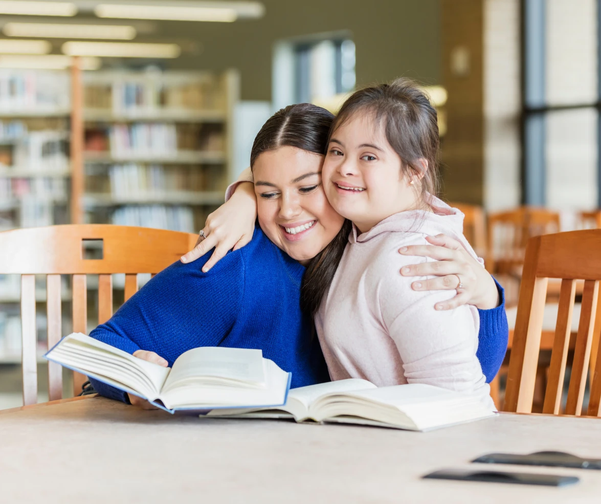 Κορίτσι με σύνδρομο Down αγκαλιάζει μια νεαρή γυναίκα σε βιβλιοθήκη